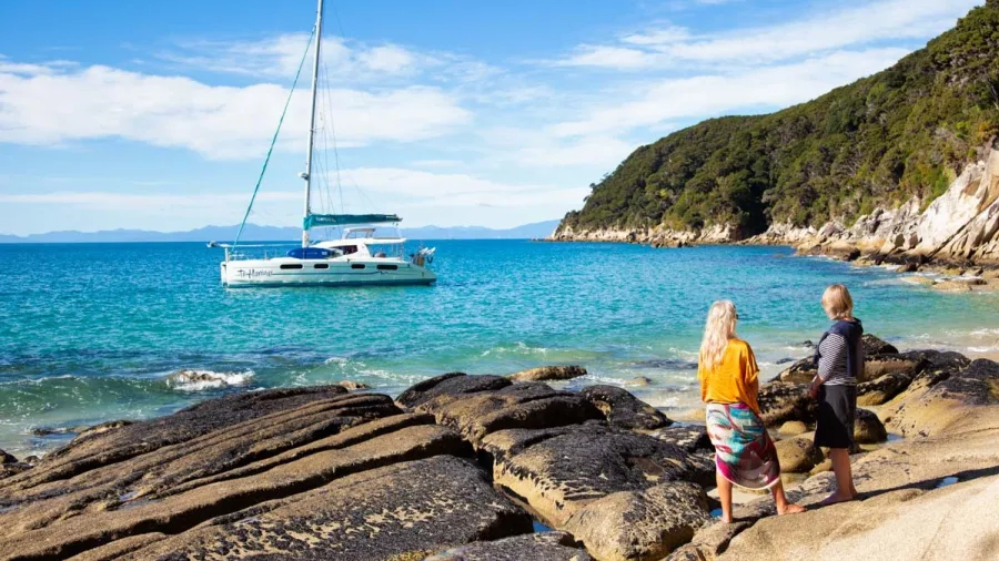 Couple on rocky beach looking out at anchored catamaran