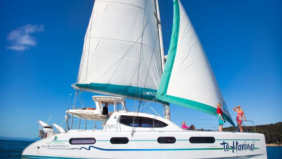 Family standing on deck of Te Harinui catamaran with full sails up