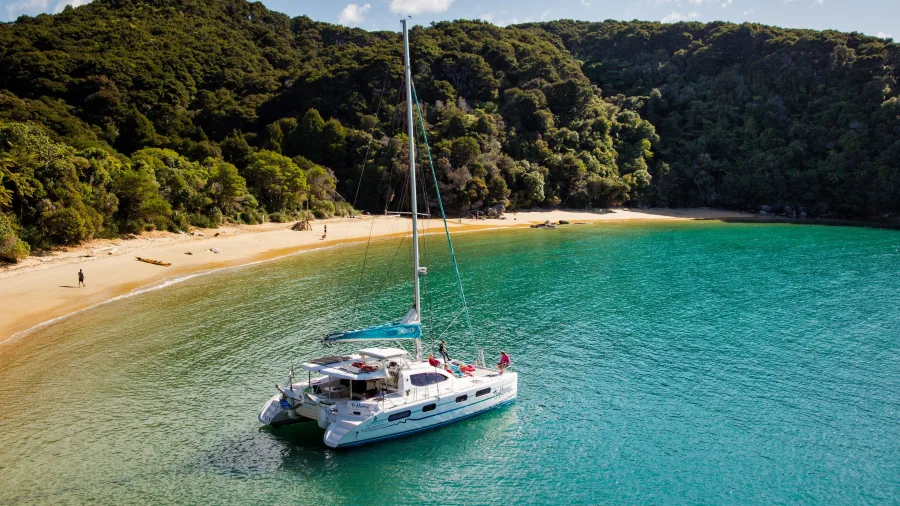 Catamaran anchored in a tranquil bay surrounded by native bush in Abel Tasman