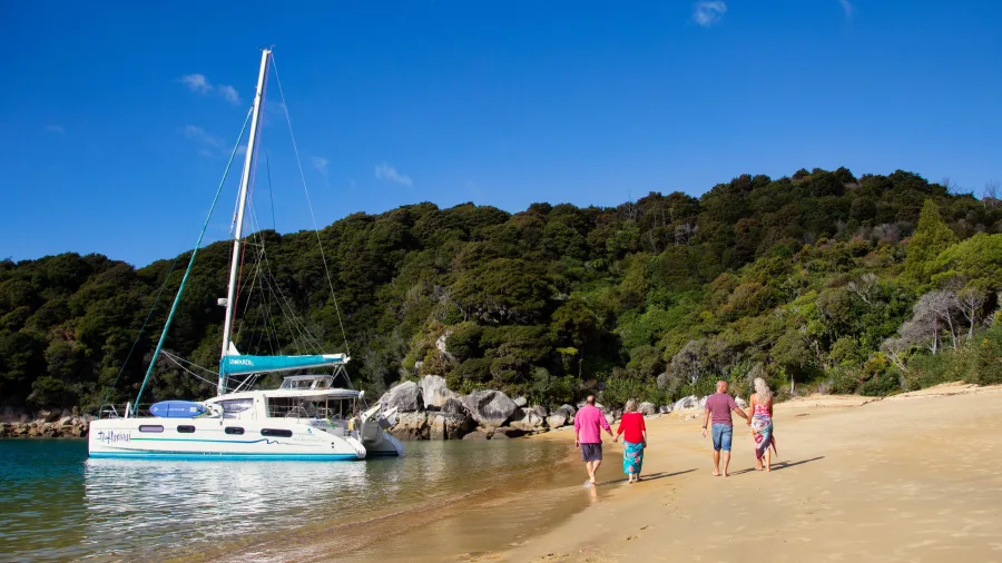 Family walking along golden sand beach with moored catamaran in Abel Tasman