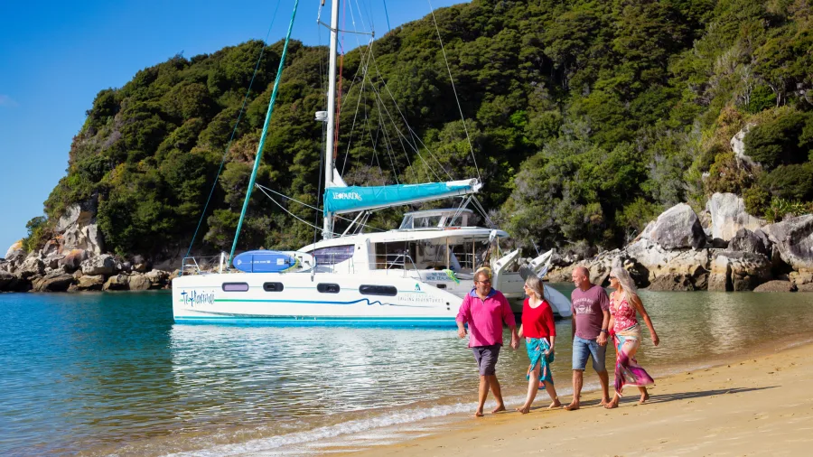 Family walking along beach with catamaran moored in calm bay