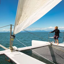 Woman enjoying the view from the front deck of a sailing catamaran in Abel Tasman