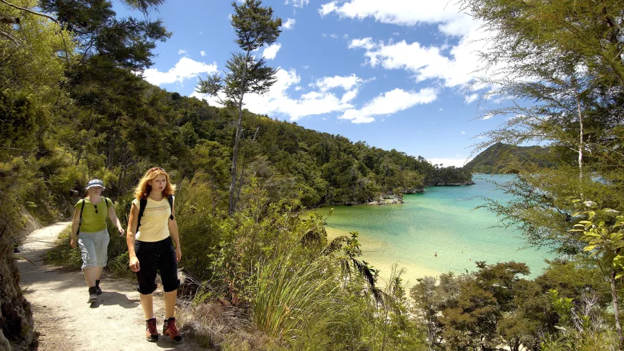 Couple hiking along the Abel Tasman Coastal Track with turquoise bay views