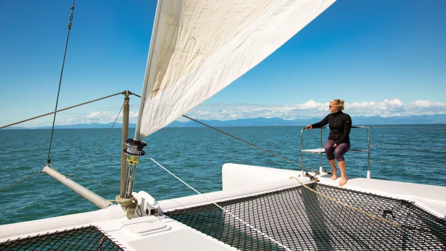 Woman enjoying the view from the front deck of a sailing catamaran in Abel Tasman