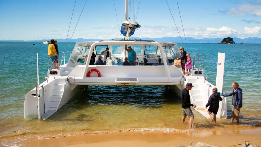 Passengers disembarking a catamaran tour on a golden Abel Tasman beach