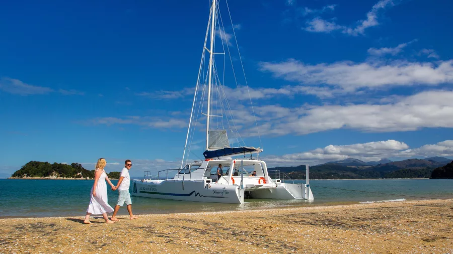 Couple walking along the beach near a catamaran in Abel Tasman