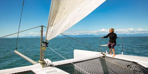 Woman enjoying the view from the front deck of a sailing catamaran in Abel Tasman