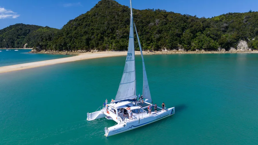 Catamaran sailing past Adele Island in Abel Tasman National Park with clear turquoise water
