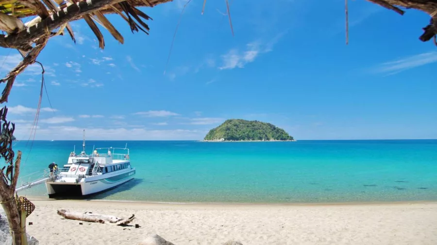 Sea shuttle docked on the white sands of Awaroa Beach with a small island in the distance and bright turquoise water