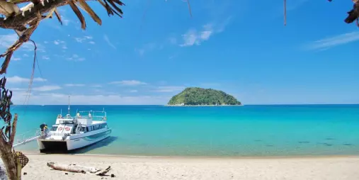 Sea shuttle docked on the white sands of Awaroa Beach with a small island in the distance and bright turquoise water