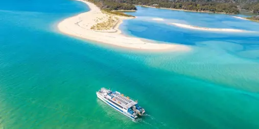 Aerial view of Abel Tasman Sea Shuttle approaching the golden sandbar of Awaroa Beach surrounded by turquoise water