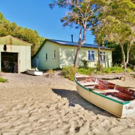Beached rowboat named Green Mary in front of a green hut and shed along Abel Tasman’s coast