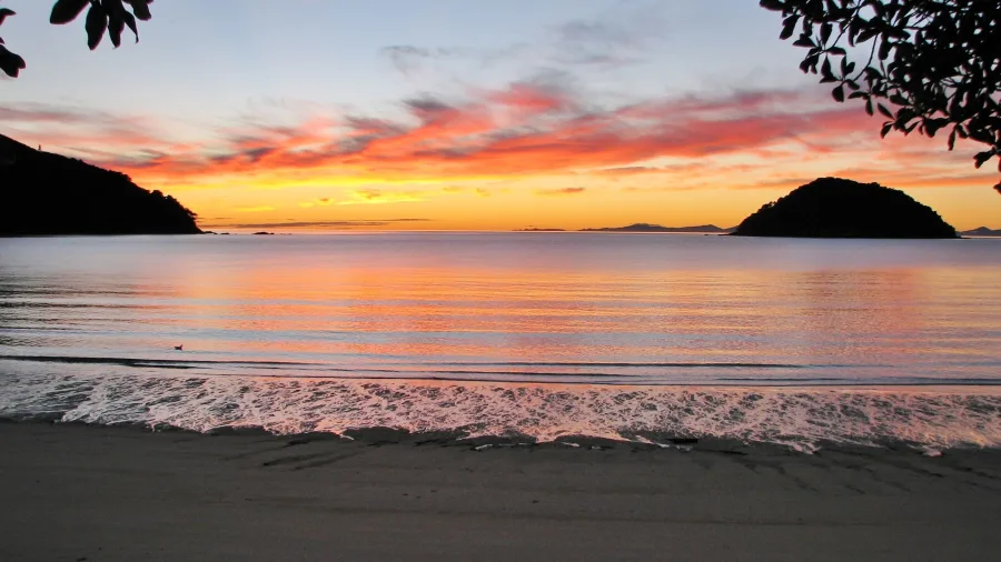 Sunrise over the calm waters of Onetahuti Beach in Abel Tasman National Park