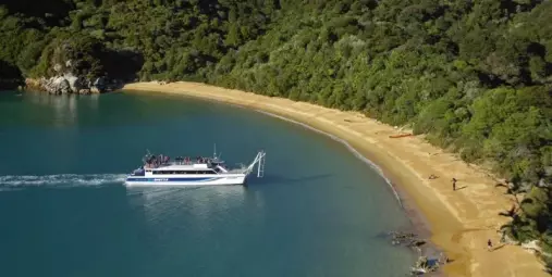 Abel Tasman Sea Shuttle boat pulling up to a golden sand beach surrounded by native bush