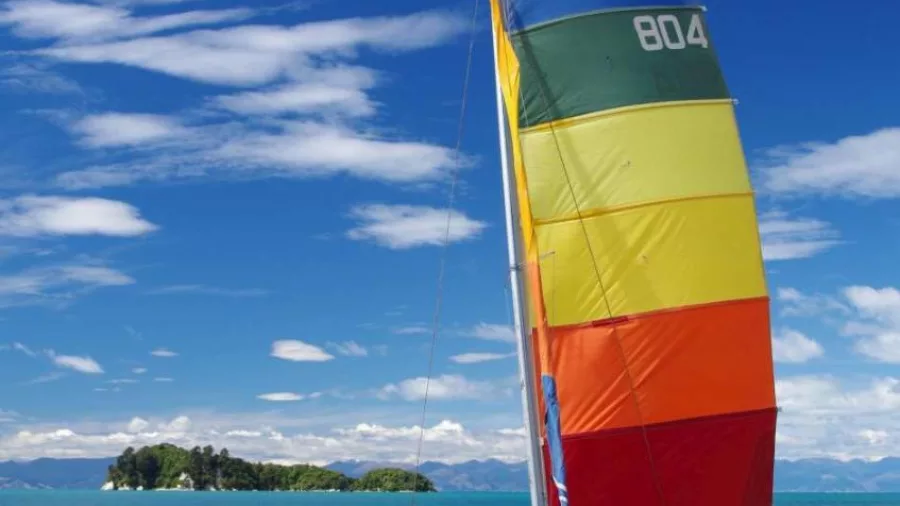 Brightly coloured catamaran with rainbow sail parked on Kaiteriteri Beach