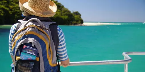 Traveller with backpack and straw hat on Sea Shuttle looking out to turquoise waters in Abel Tasman
