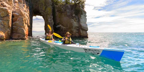 Two people kayaking through granite arch in Wainui Bay with Golden Bay Kayaks