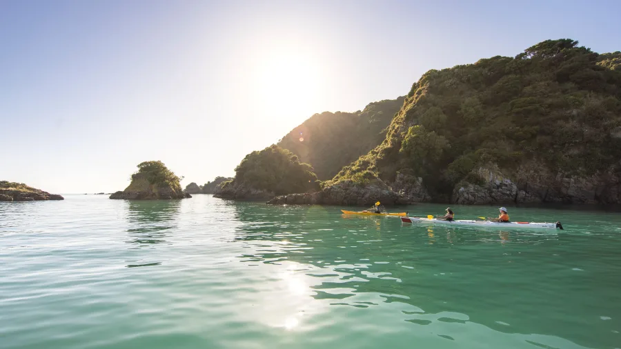 Kayakers paddling past rocky islets in Golden Bay at sunset