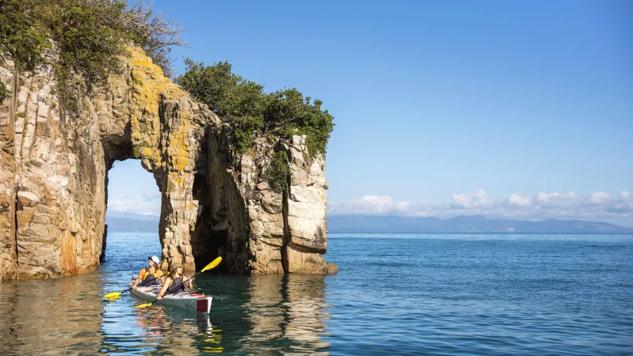 Kayakers paddling through a natural sea arch at Abel Tasman Point