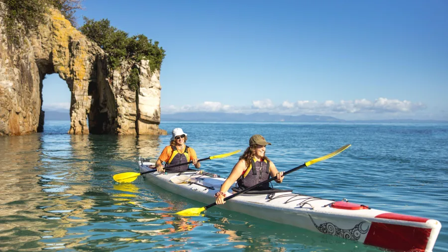 Two kayakers paddling past the sea arch at Abel Tasman Point