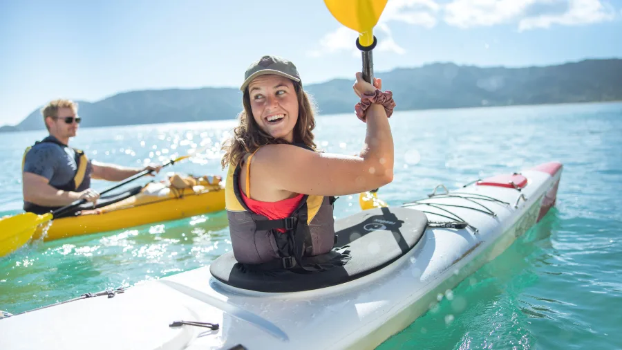 Woman smiling while kayaking on clear turquoise water in Golden Bay