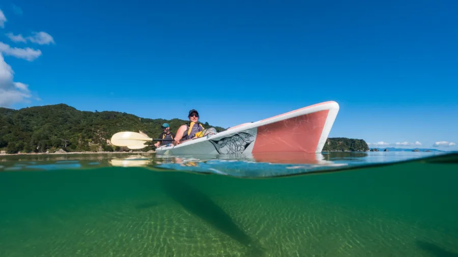 Kayakers in clear green water at Golden Bay, New Zealand, captured above and below waterline