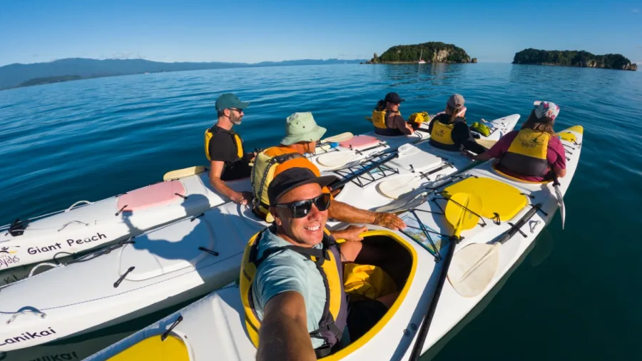 Group of kayakers smiling and paddling together across calm sea in Golden Bay