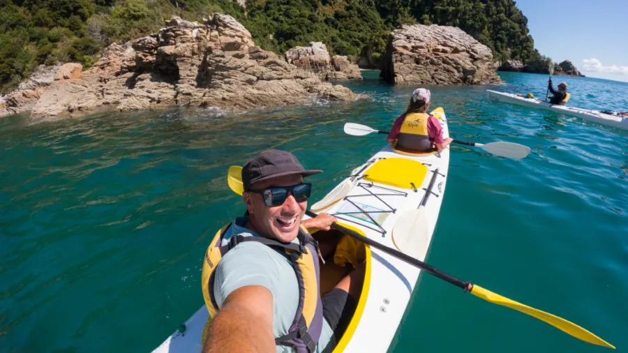 Smiling kayaker taking a selfie during a guided Golden Bay Kayaks tour near rocky coastline