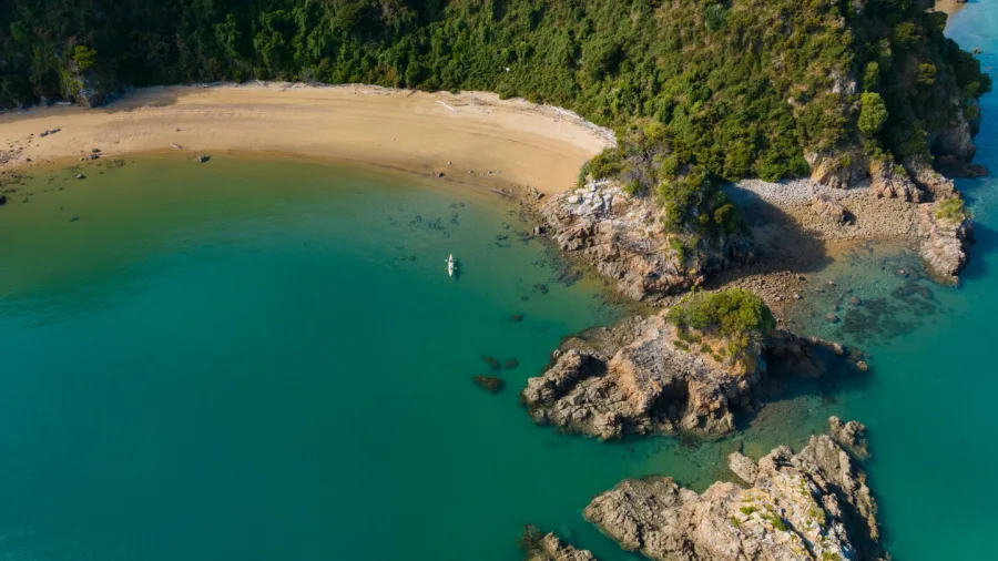 Aerial view of a kayak near a secluded beach and rocky coastline in Golden Bay, New Zealand