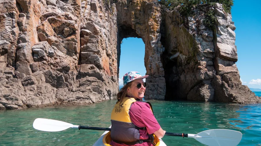 Smiling kayaker in front of a natural rock arch at Golden Bay