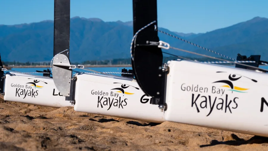 Golden Bay Kayaks outriggers resting on sand with mountain range in background