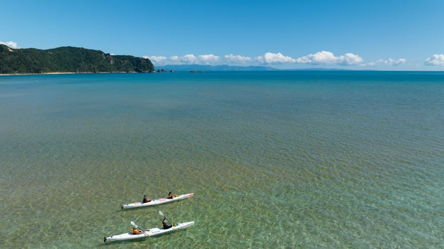 Drone view of kayakers paddling through clear shallow waters in Golden Bay