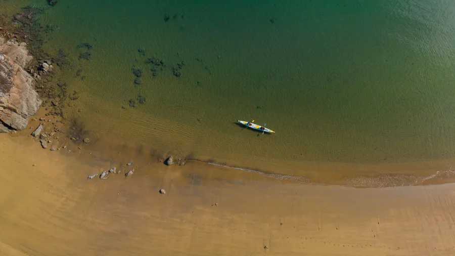 Aerial view of a double kayak landing on the golden sandy shore of Golden Bay