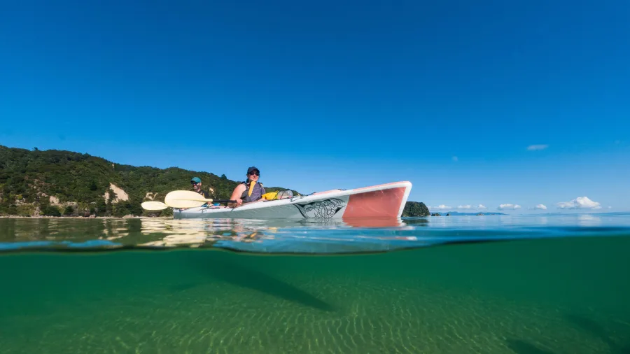 Two kayakers paddling on crystal-clear water with part of the kayak visible underwater