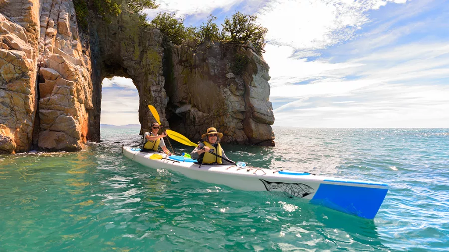 Two people kayaking through granite arch in Wainui Bay with Golden Bay Kayaks