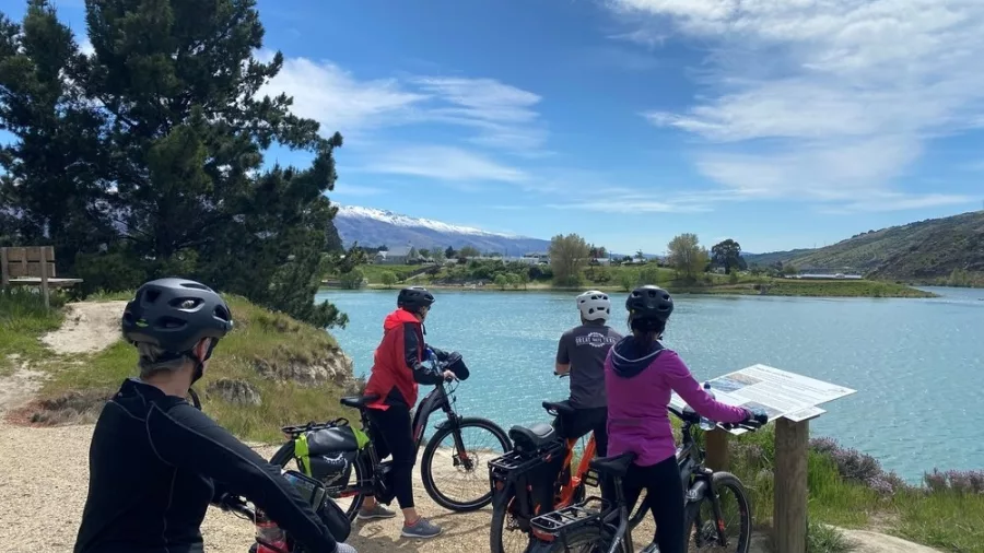 Group of cyclists stopping to read an information sign beside a lake in Cromwell with mountain views