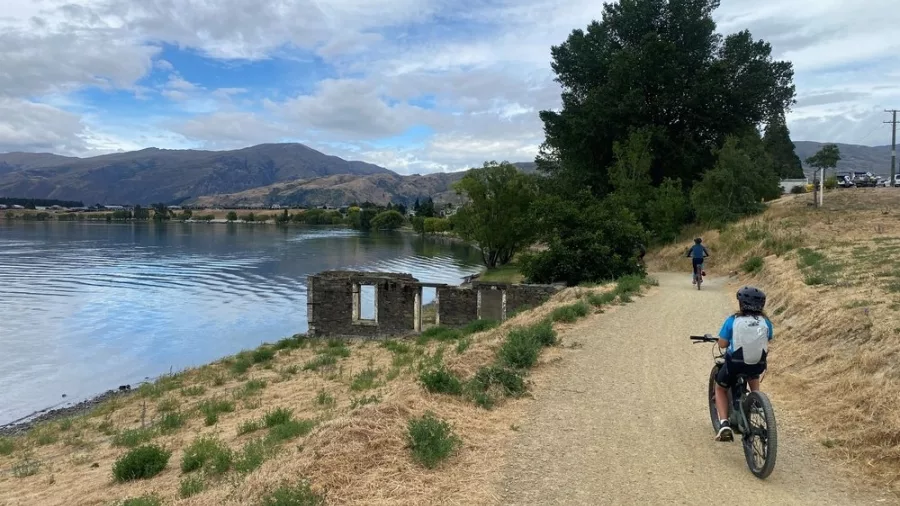 Cyclists riding past historic stone ruins along the lakeside trail in Cromwell