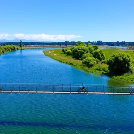 Cyclists crossing a suspension bridge over a calm river on the Nelson to Mapua trail