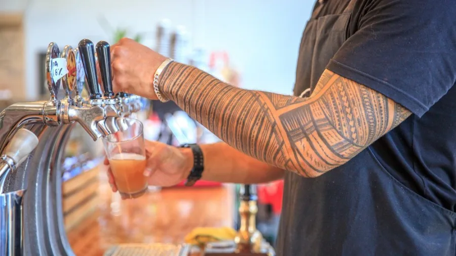 Bartender with traditional tattoo pouring craft beer from tap