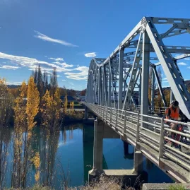 Cyclist crossing metal bridge along the Roxburgh Gorge Trail in autumn