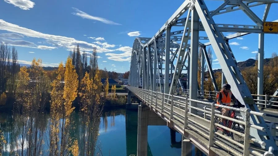 Cyclist crossing metal bridge along the Roxburgh Gorge Trail in autumn