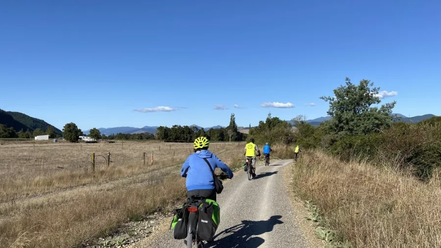 Group of cyclists biking along a gravel trail in rural Nelson with blue skies