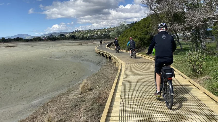 Cyclists riding along a wooden boardwalk beside the coast on the Tunnel to Town route with Kiwi Journeys