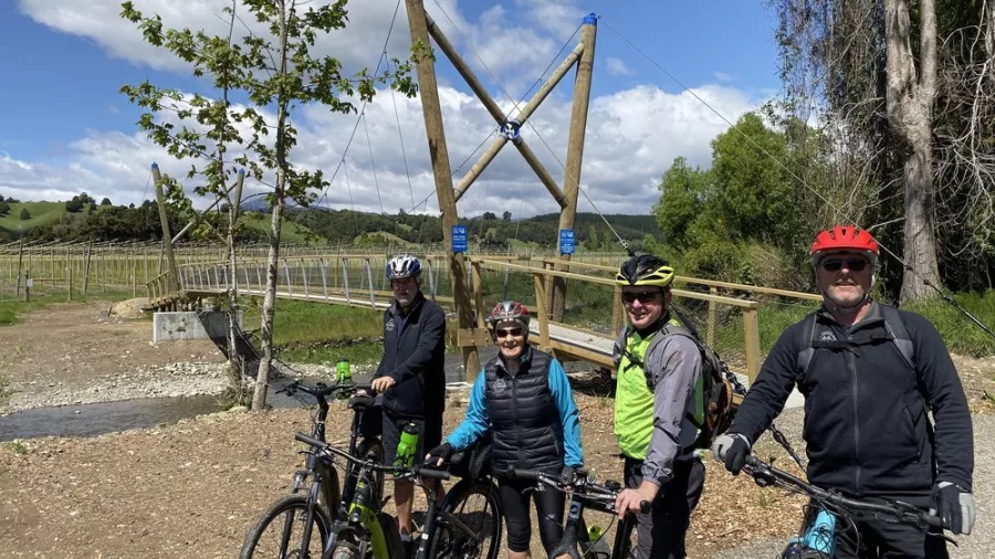 Group of cyclists standing beside their bikes near a wooden suspension bridge on the Tunnel to Town route with Kiwi Journeys