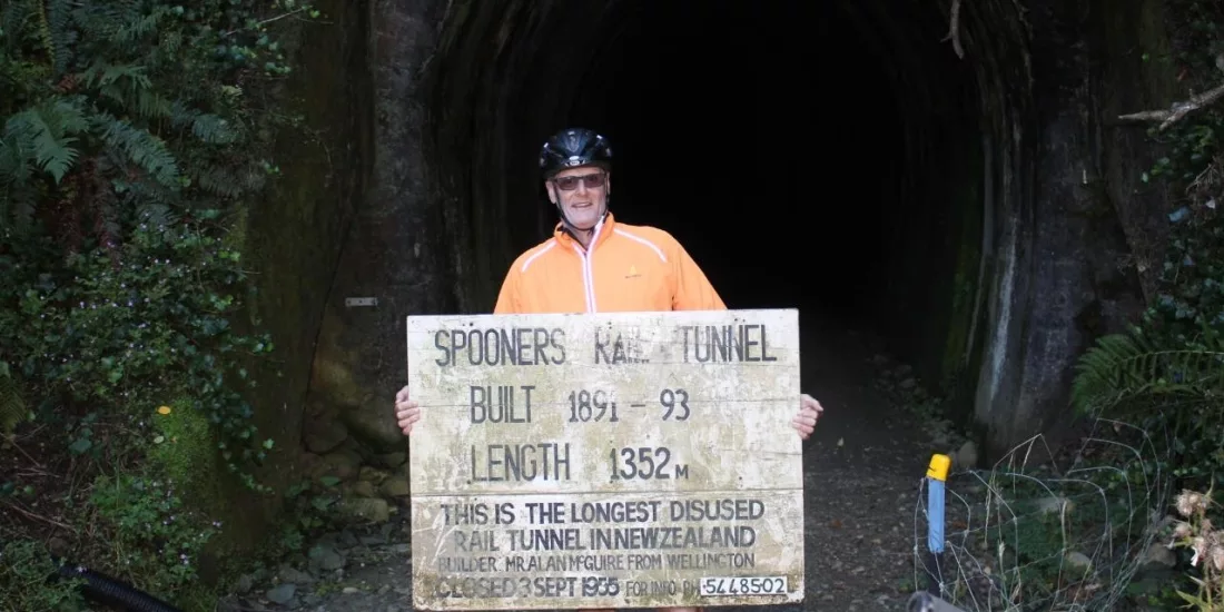 Cyclist holding Spooners Tunnel sign at the tunnel entrance on the Great Taste Trail