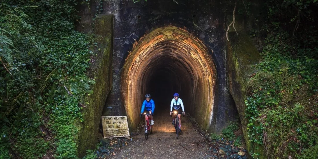 Two cyclists with headlights exiting Spooners Tunnel on the Mapua trail with Kiwi Journeys