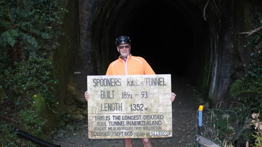 Cyclist holding Spooners Tunnel sign at the tunnel entrance on the Great Taste Trail