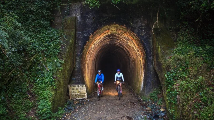 Two cyclists with headlights exiting Spooners Tunnel on the Mapua trail with Kiwi Journeys