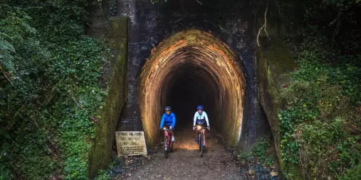 Two cyclists with headlights exiting Spooners Tunnel on the Mapua trail with Kiwi Journeys