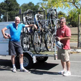 Two cyclists beside a Nelson Cycle Hire trailer loaded with bikes
